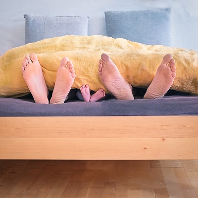 Cold Feet: Six uncovered feet at the foot of a bed