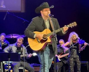 Foot in the Door--Collin White with guitar, jeans, jacket, and cowboy hat